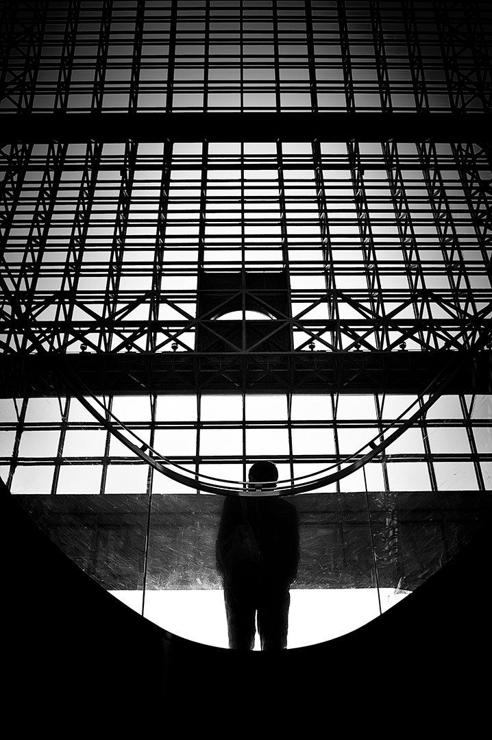 Una figura en sombra bajo una cubierta de estructura reticulada.